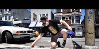 LGBTQ Artist Speaks Out After Homophobic Attacks On His Milwaukee Artwork Male street artist wearing a cap and face mask crouches on a city sidewalk, spray-painting orange art with cans nearby and cars in the background