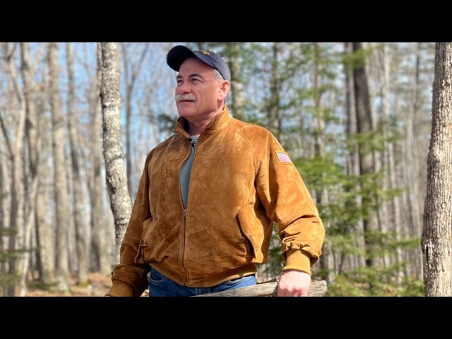 Maine GOP Candidate Cites Noah’s Ark to Deny the Existence of Transgender Youth Older man with a mustache wearing a brown suede jacket and cap stands in a bare forest, looking into the distance.