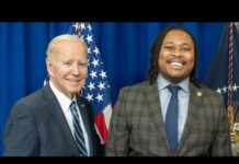 Biden Honored for LGBTQ+ Advocacy at Philadelphia Stonewall Awards During Pride Month Two men in suits posing for a photo in front of American flags, smiling at the camera.