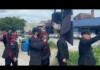 Nazi Symbols, Hate Speech Disrupt Downtown Parade Celebration at Athens Pride Group of men in black suits with red shirts and masks stand on a sidewalk; one salutes while a large black-and-white flag is raised nearby.