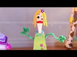 Stop-motion puppet with yellow yarn hair, green pipe-cleaner arms, and a lime dress, making a surprised expression in a play scene.