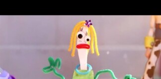Stop-motion puppet with yellow yarn hair, green pipe-cleaner arms, and a lime dress, making a surprised expression in a play scene.