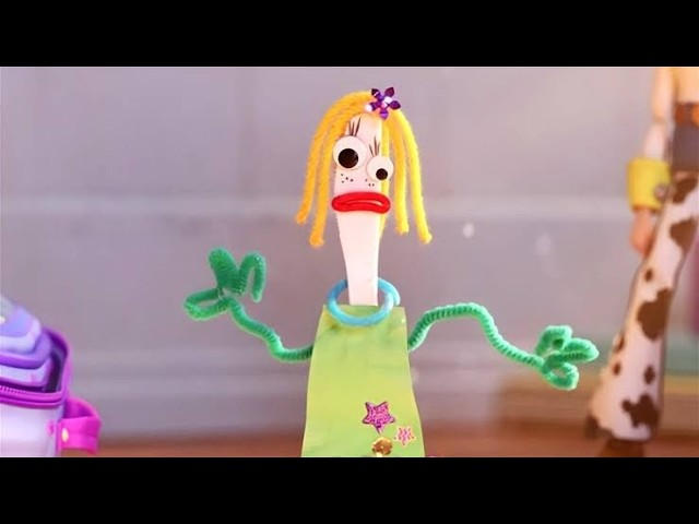 Stop-motion puppet with yellow yarn hair, green pipe-cleaner arms, and a lime dress, making a surprised expression in a play scene.