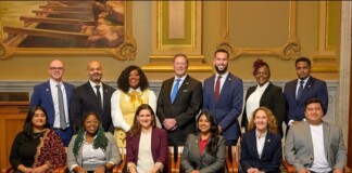 Formal group photo: 12 diverse professionals posed in three rows in a grand, ornate room.