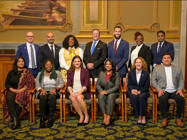 Formal group photo: 12 diverse professionals posed in three rows in a grand, ornate room.