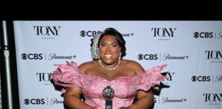 Plus-size woman in a pink off-shoulder gown holding a Tony Award on a red carpet backdrop with CBS and Paramount+ logos.