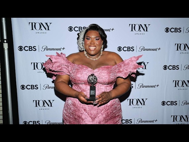 Plus-size woman in a pink off-shoulder gown holding a Tony Award on a red carpet backdrop with CBS and Paramount+ logos.