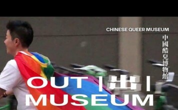 Person walking past a banner wearing a rainbow Pride flag; large white text reads 'OUT MUSEUM' with vertical Chinese text 'CHINESE QUEER MUSEUM' on the right.