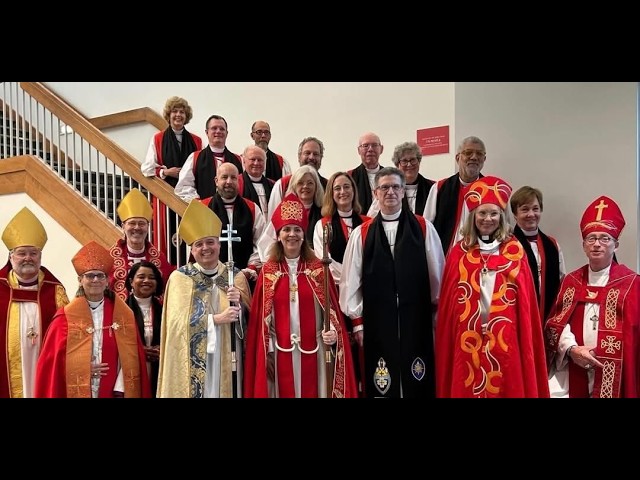 Southern Episcopal Diocese Appoints First Openly Lesbian Bishop in Historic Milestone Group of clergy in red, gold, and white liturgical vestments posing for a group photo on a stairwell in a church setting.