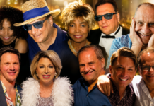 Group of ten adults smiling for a party photo, wearing colorful outfits against a golden bokeh backdrop.