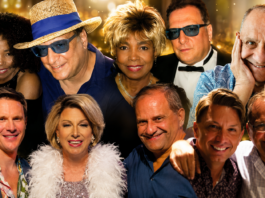From The Publisher: A Week of Profound Loss Group of ten adults smiling for a party photo, wearing colorful outfits against a golden bokeh backdrop.