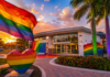Rainbow flag waves above a rainbow-painted plaza in front of a modern building at sunset for a Pride-themed scene.