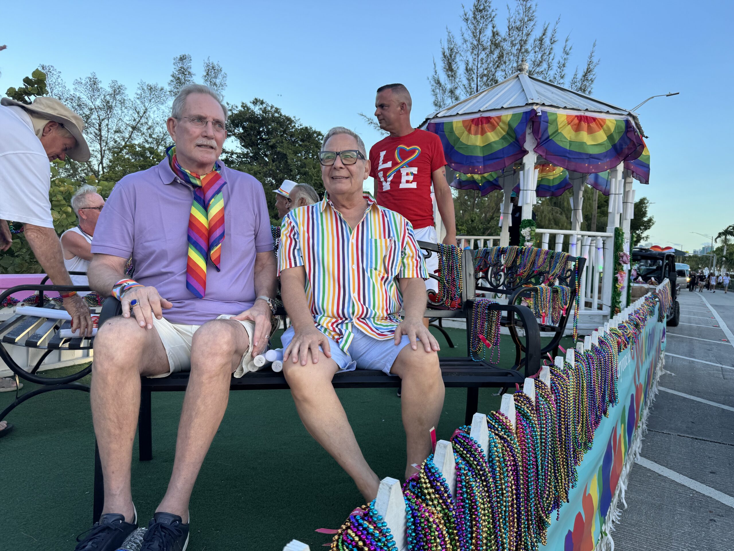 Paul Rolli: Ready to Lead Wilton Manors Into Its Next Chapter | Hotspots Magazine Hotspots Magazine People riding on a pride parade float wearing colorful outfits and rainbow accessories, with bead garlands on display behind them.