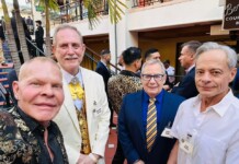 Four men in suits posing for a selfie at an outdoor event, name badges visible on each attendee.