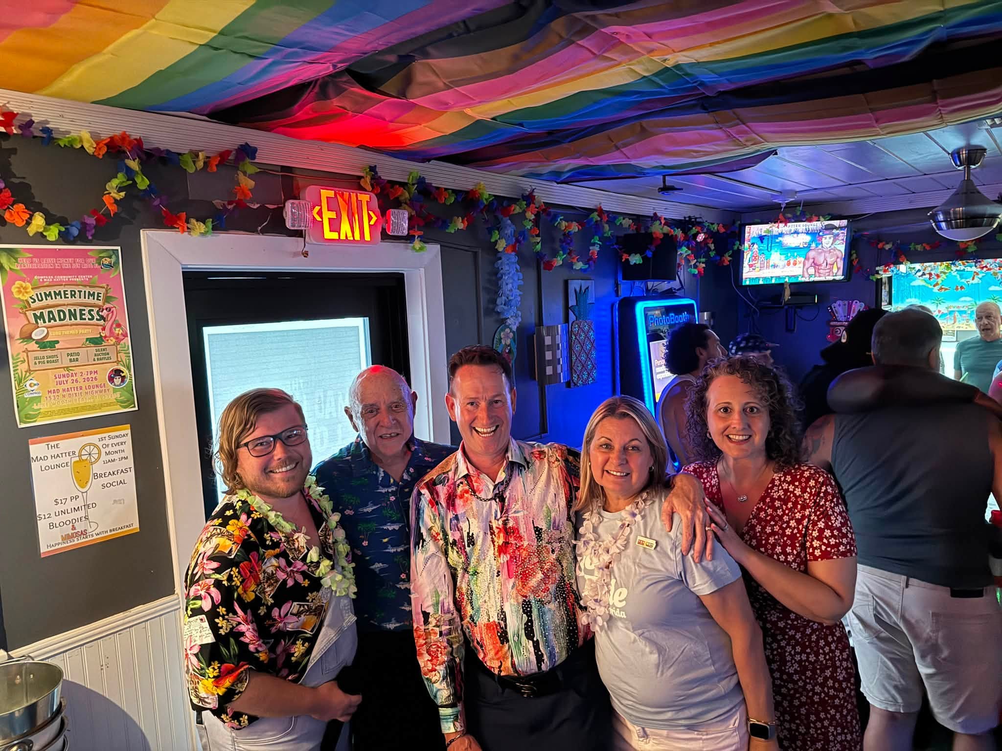 Out With Scott – By Scott Holland | Hotspots Magazine Hotspots Magazine Smiling group of adults in tropical shirts posing in a colorful party room with rainbow fabric ceiling and leis.