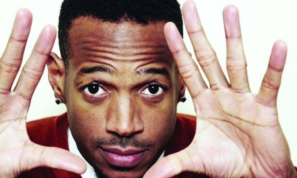 Man holds his hands up and frames his face, looking directly at the camera.