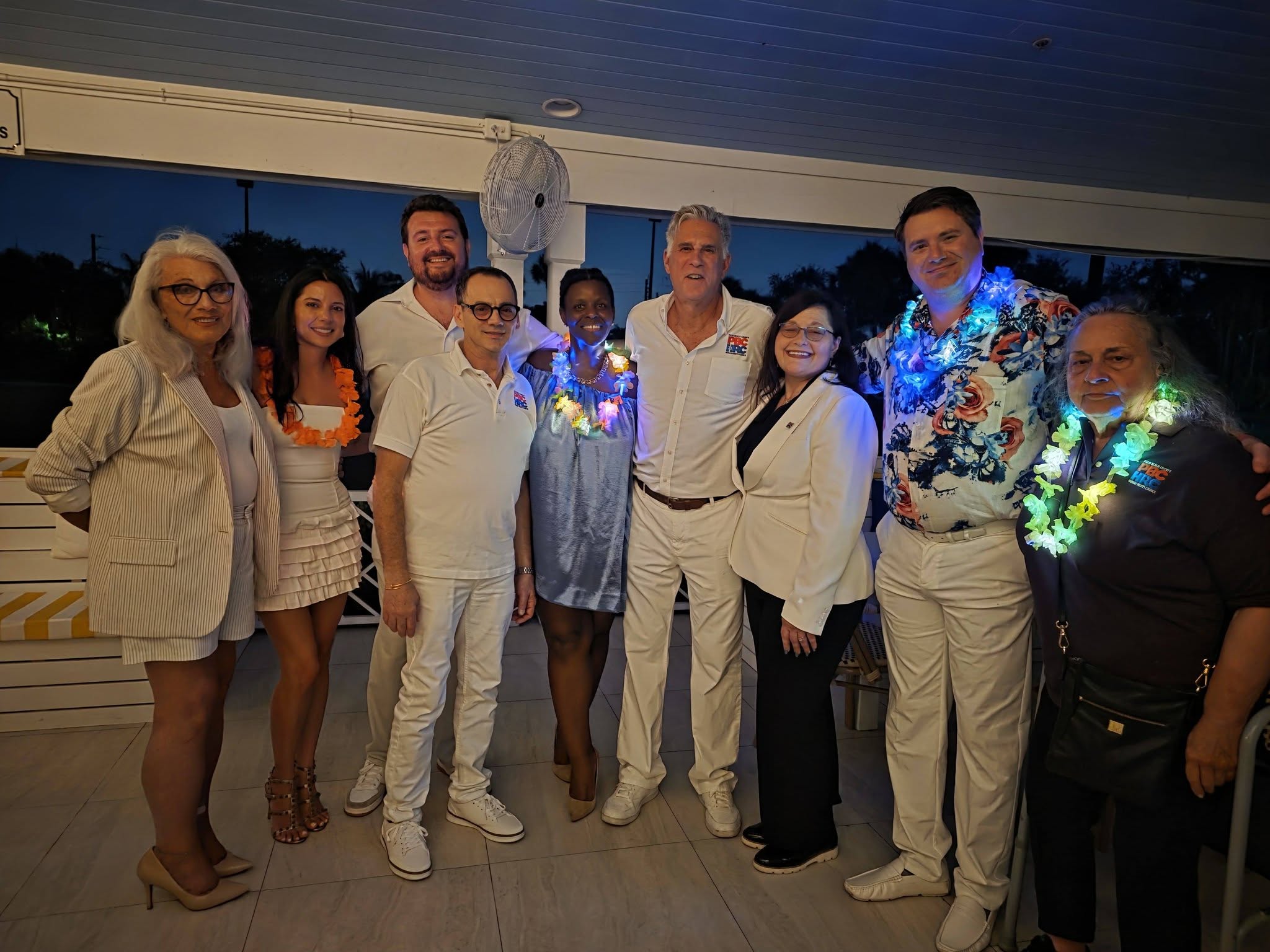 Out With Scott – By Scott Holland | Hotspots Magazine Hotspots Magazine Group of adults posing together at a party, all in white outfits with colorful leis and glowing lights.