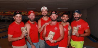 Six men in red shirts pose together in a bowling alley, each holding a brochure or flyer with a shirt logo visible in the background lanes.