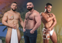 Three shirtless men posing on a tropical beach; left holds a towel, middle wears jeans, right wears white harness-style underwear.