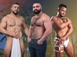 Three shirtless men posing on a tropical beach; left holds a towel, middle wears jeans, right wears white harness-style underwear.