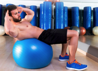 Focus on the Prize: How to Stay Focused on Your Fitness Goals Man performing an abdominal crunch on a blue stability ball in a gym with mirrors and equipment in the background.