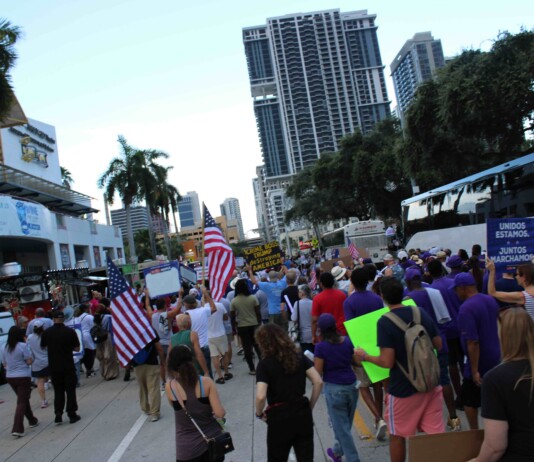Out With Scott: By Scott Holland Crowd of protesters marching on a city street, many waving American flags and holding signs.