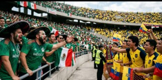 Energetic soccer fans in green Mexico jerseys chant at a stadium barrier, with Mexican and Ecuadorian flags nearby.