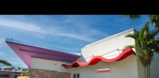 Exterior of a white commercial building with a red wavy canopy, brick accents, and ramp access under a blue sky.