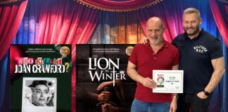 Two men pose with colorful stage posters for Island City Stage productions: 'Who Killed Joan Crawford?' and 'The Lion in Winter'.
