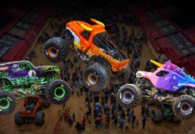 Monster Jam Returns to Amerant Arena – Saturday and Sunday Aug 22 & 23 Three colorful monster trucks mid-air over a dirt arena as a crowd watches a high-energy show.