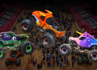 Monster Jam Returns to Amerant Arena – Saturday and Sunday Aug 22 & 23 Three colorful monster trucks mid-air over a dirt arena as a crowd watches a high-energy show.