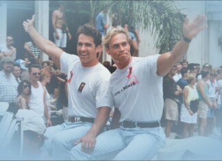 Deep Inside Hollywood: A Bloody Prom, Queer Bodybuilders, and the Return of the ’90s Supers Two men in white T-shirts ride a boat and wave to a cheering crowd at a sunny parade.