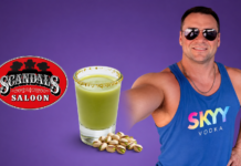 Man in sunglasses and a blue SKYY Vodka tank top poses with a green salted-rim drink and pistachios beside a Scandal's Saloon logo on a purple background.