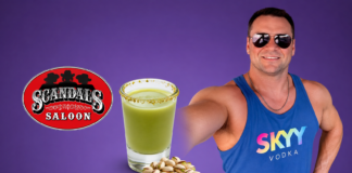 Hot Bartender – Joe Payne Man in sunglasses and a blue SKYY Vodka tank top poses with a green salted-rim drink and pistachios beside a Scandal's Saloon logo on a purple background.