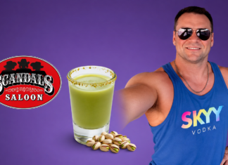 Hot Bartender – Joe Payne Man in sunglasses and a blue SKYY Vodka tank top poses with a green salted-rim drink and pistachios beside a Scandal's Saloon logo on a purple background.
