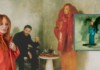 Red-haired woman in an orange coat stands at left; a man in black sits behind beside a table with glasses, against a moody green backdrop; an inset album cover appears on the right.