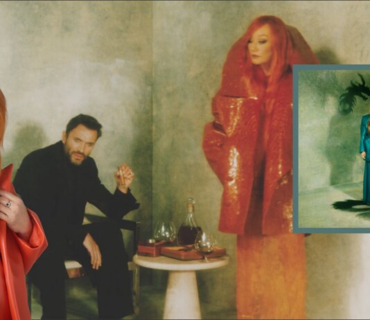 Red-haired woman in an orange coat stands at left; a man in black sits behind beside a table with glasses, against a moody green backdrop; an inset album cover appears on the right.