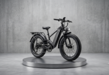 Business Profile – Carvelle Bikes: Keeping Wilton Manors Rolling – One Rider at a Time Black electric bike on a round metallic pedestal in a minimalist concrete studio setting.
