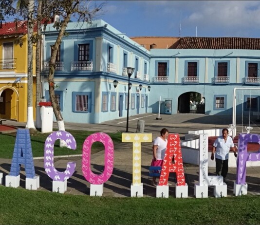 Genre Latino: Veracruz, Mexico Colorful outdoor letters spell Tlacotalpan in front of pastel colonial buildings on a sunny plaza, Veracruz.
