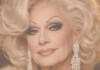 Close-up portrait of a glamorous older woman with platinum blonde hair and diamond earrings.
