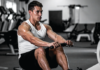Muscular man in a white tank top rows a cable handle in a gym, focused on the exercise.