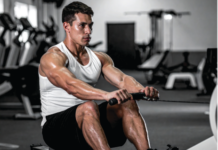 Boost It Naturally: Top 12 Natural Testosterone Boosters Muscular man in a white tank top rows a cable handle in a gym, focused on the exercise.