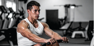 Muscular man in a white tank top rows a cable handle in a gym, focused on the exercise.