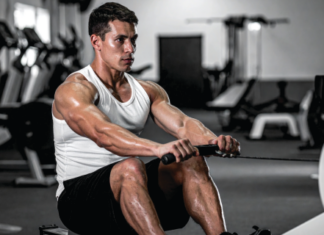 Muscular man in a white tank top rows a cable handle in a gym, focused on the exercise.