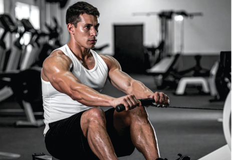 Boost It Naturally: Top 12 Natural Testosterone Boosters Muscular man in a white tank top rows a cable handle in a gym, focused on the exercise.