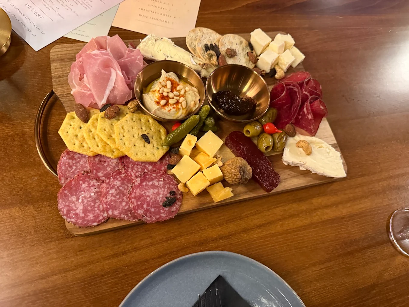 Charcuterie board with assorted meats, cheeses, crackers, olives, and dips on a wooden platter.