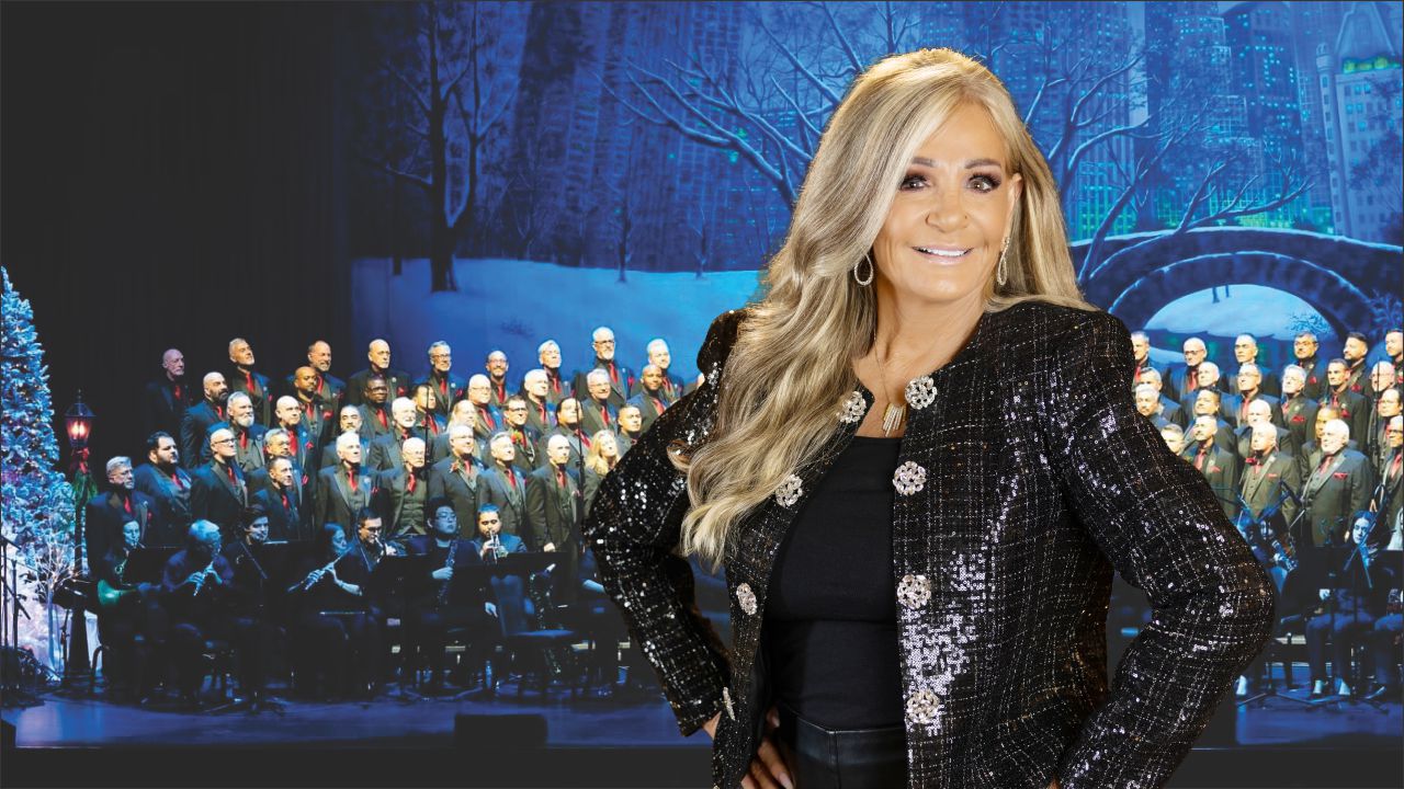 Woman in a glittery black jacket poses at the front of a choir on stage with a snowy blue backdrop.