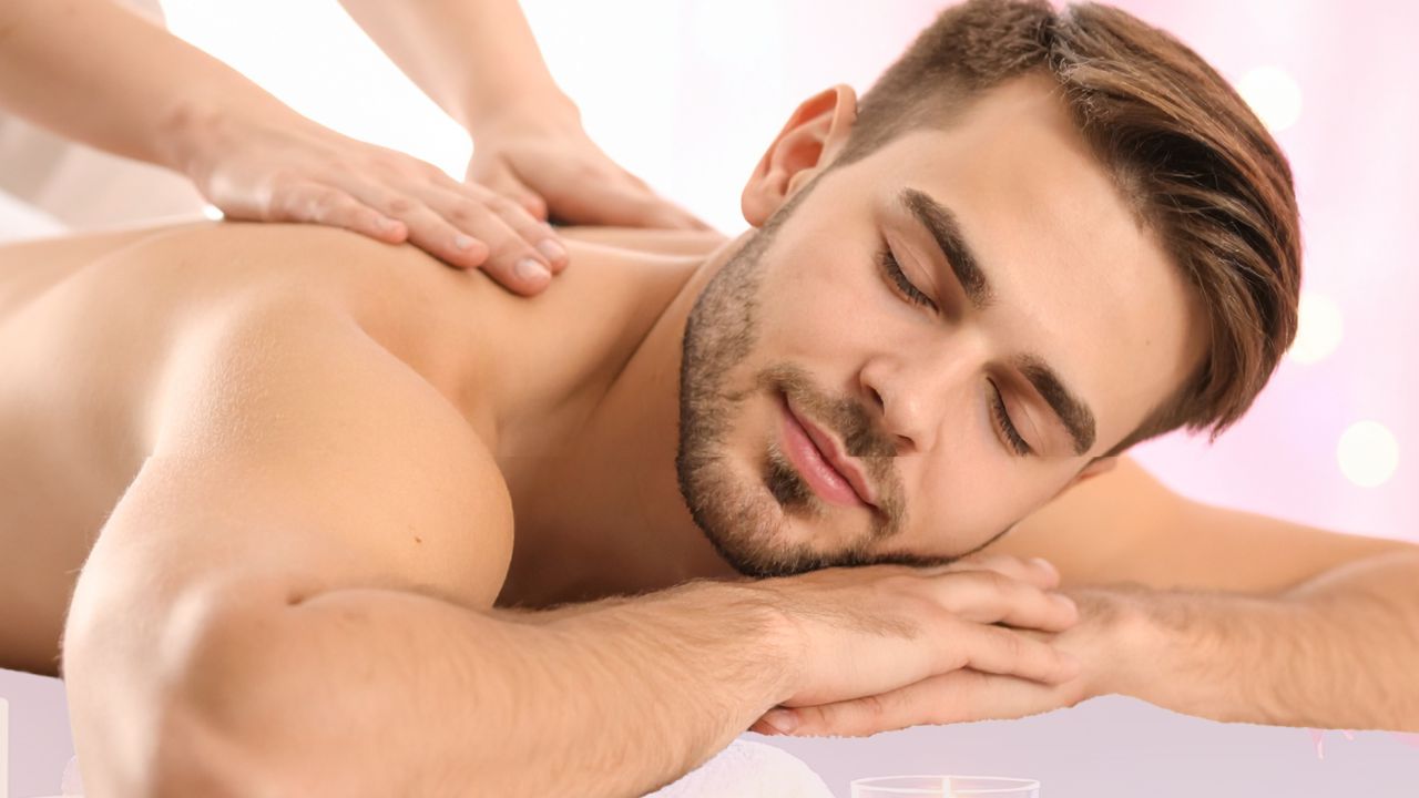 Relaxed man receiving a back massage in a spa, eyes closed and face resting on a pillow or folded arms.